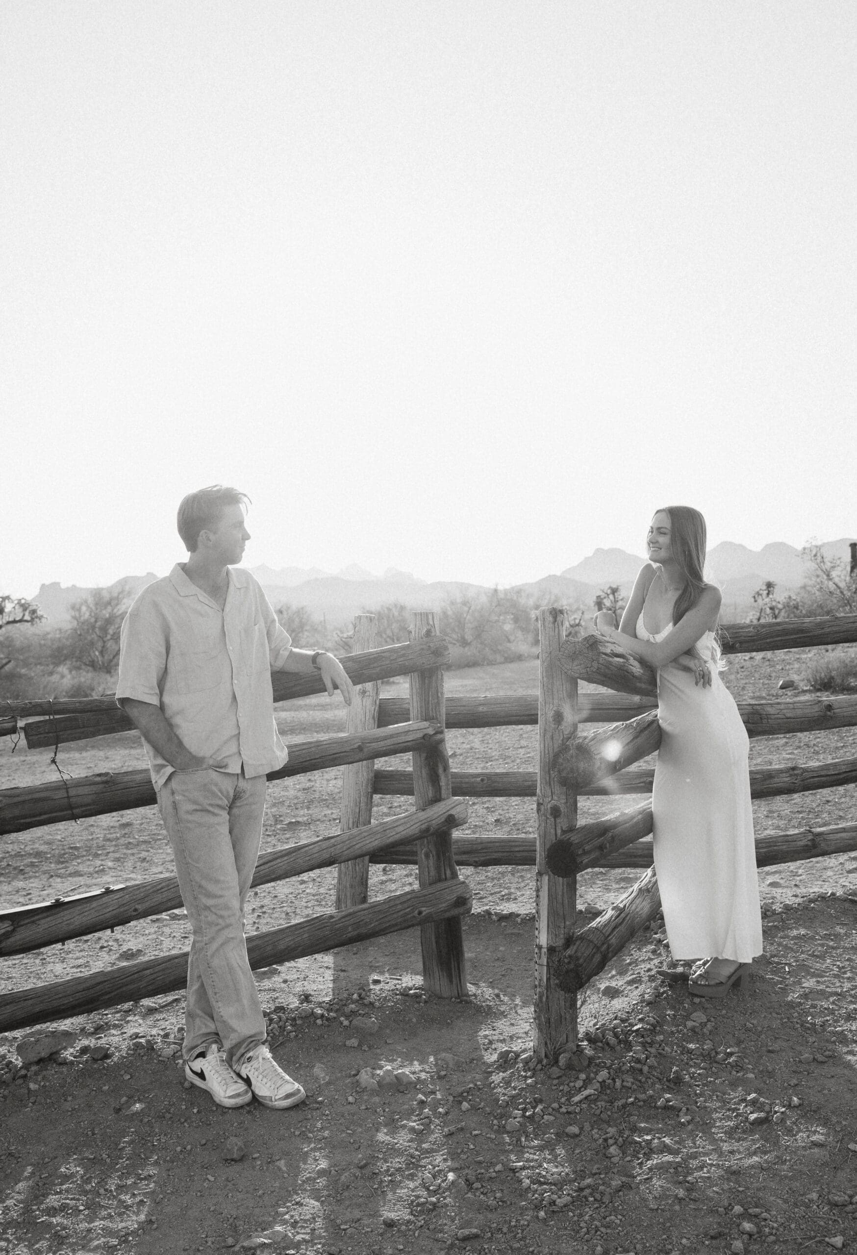 couple-leaning-on-fence-smiling-at-each-other-in-arizona-desert